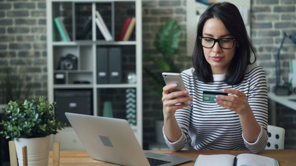 woman checking broadband price on phone and laptop